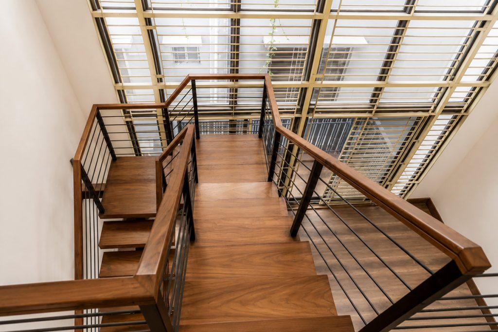 Wooden staircase with steel railing under a double-height glass and jali screen wall in a duplex residence interior, Bashundhara, Dhaka