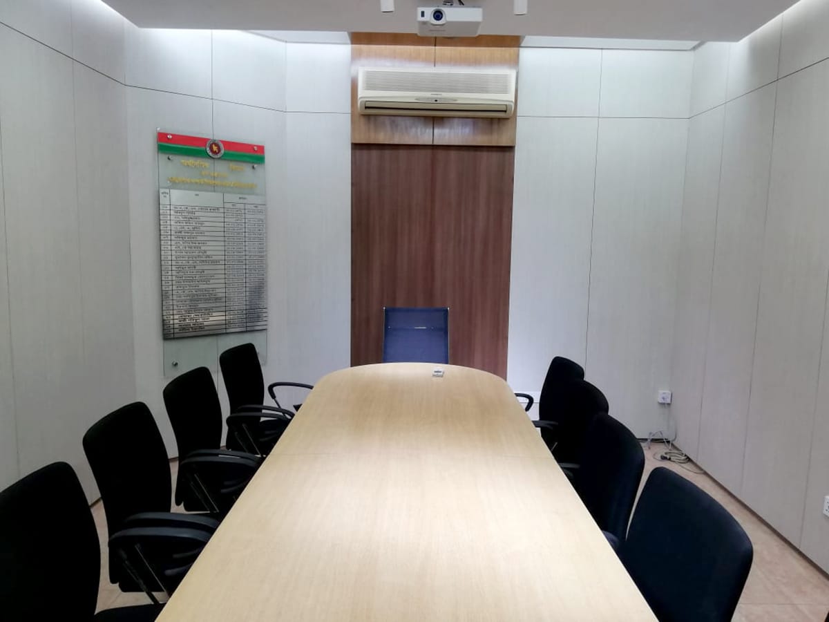 Small conference room with oval meeting table, ceiling-mounted projector and wood accent wall, K4DM, Planning Ministry, Dhaka