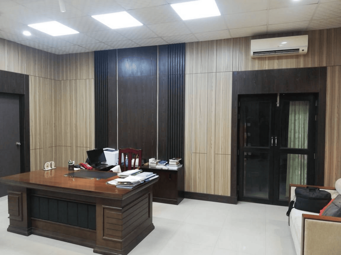 Executive desk with dark wood panel accent wall and glass door in Wing Chief office interior, Planning Commission, Dhaka