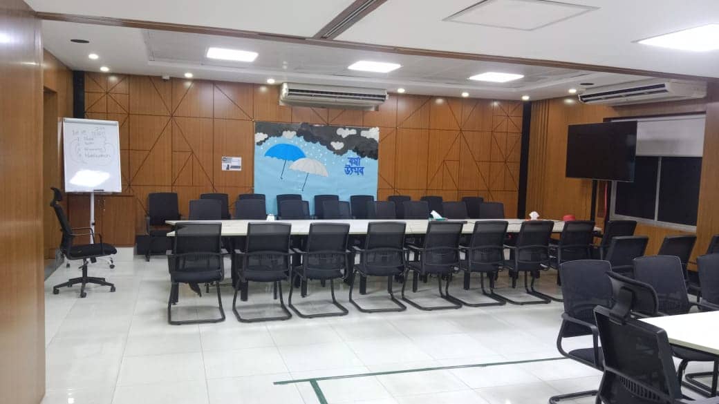 Training room with rows of chairs, wood-paneled wall and display screen, A2i Paribahan Pool office interior design in Segunbagicha, Dhaka
