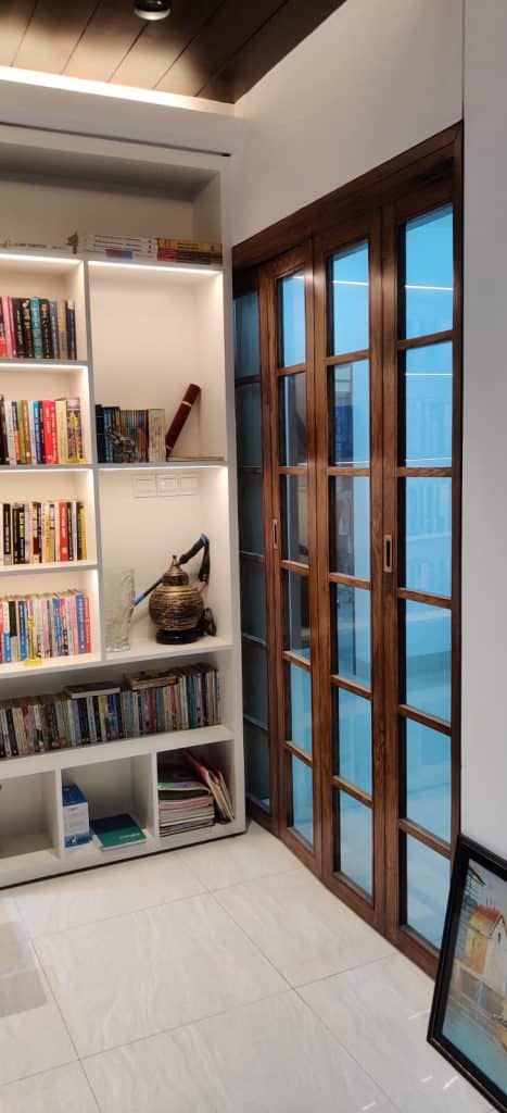 Tall bookshelf with books and decor beside a wooden-frame glass folding door - residence interior design in Rampura, Dhaka